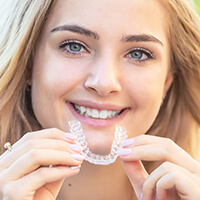 ortho-invisalign teenage girl holding up a clear aligner